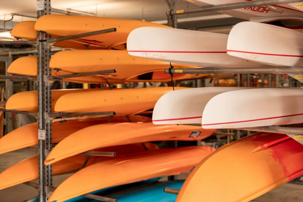 Orange and white kayaks stored upside down on metal rack arms indoors