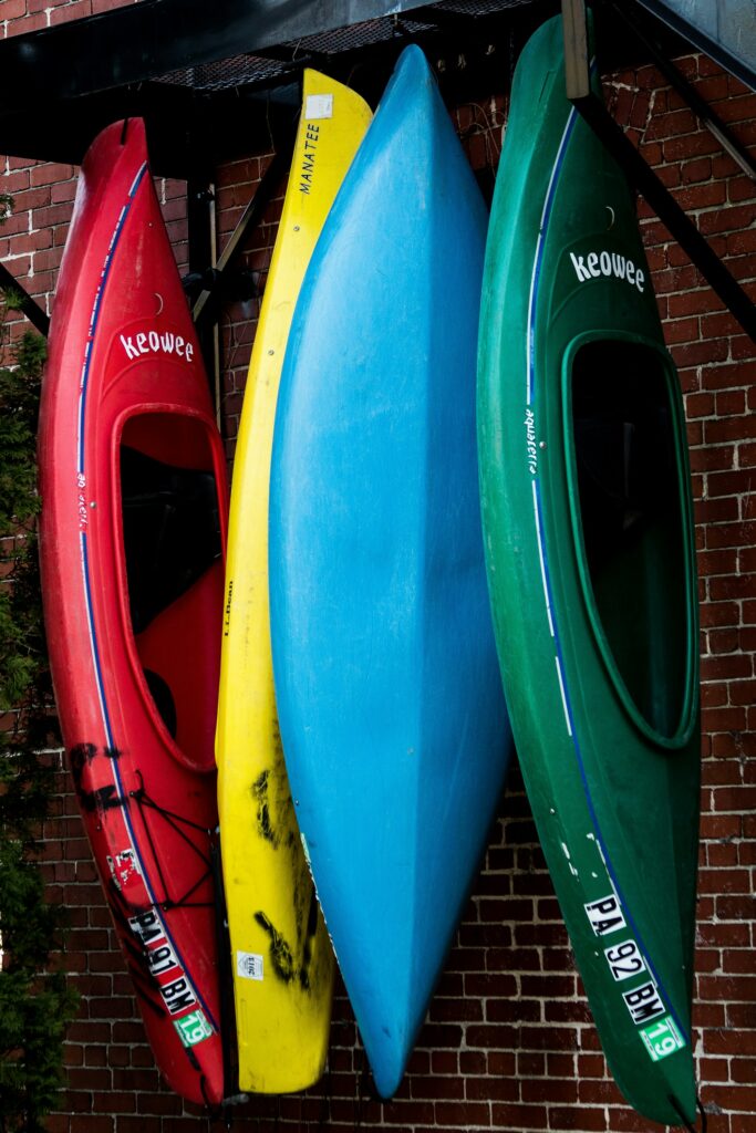 Four plastic kayaks, red, yellow, blue and green, stored standing on end against a brick wall