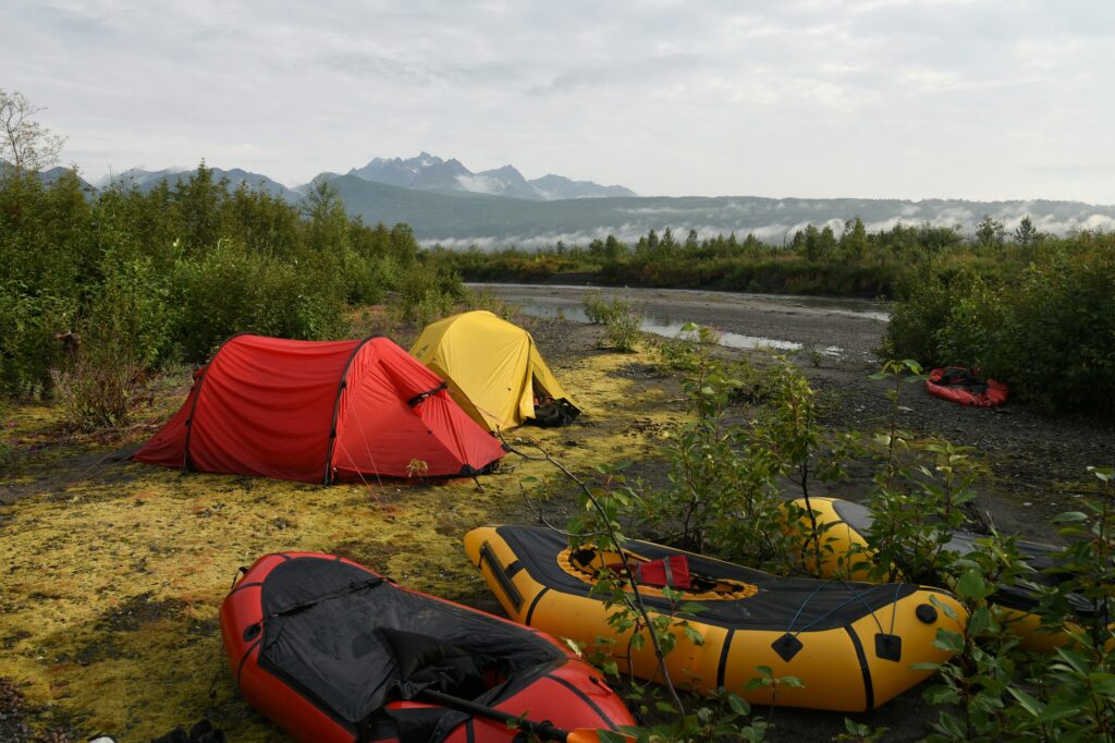 Red and yellow inflatable packrafts on a riverbank beside two tents