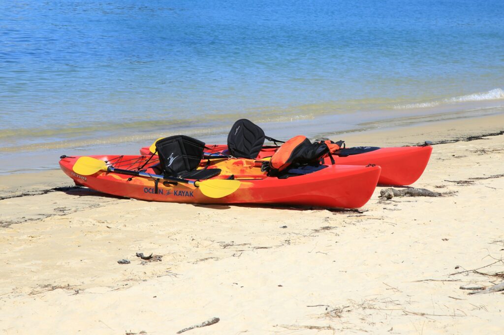 Two red Ocean Kayak sit-on-top kayaks with seat backs and a paddle pulled up on a sandy beach
