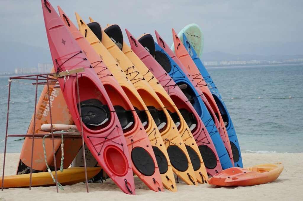 A row of red, yellow and blue sit-on-top kayaks standing on end against a metal rack on a beach