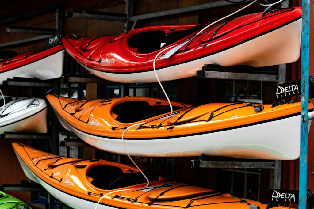 Red and orange touring kayaks resting on padded rack arms in a shop, a cable lock run through them