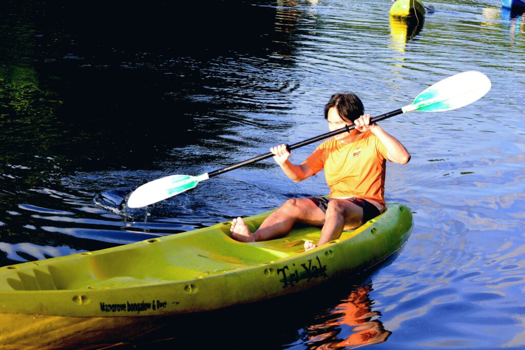 A paddler sitting on top of an open green sit-on-top kayak, feet in the molded footwells